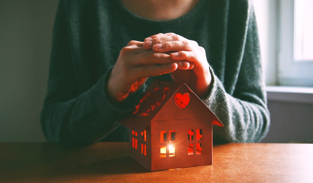 Woman holding hands over wooden home with candle inside