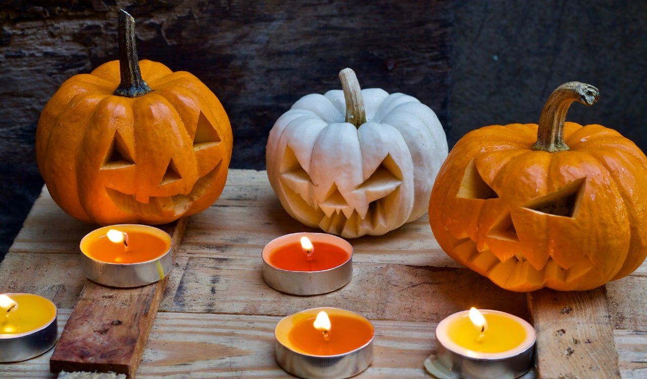 Jack-o-lanterns on wooden table with tea lights